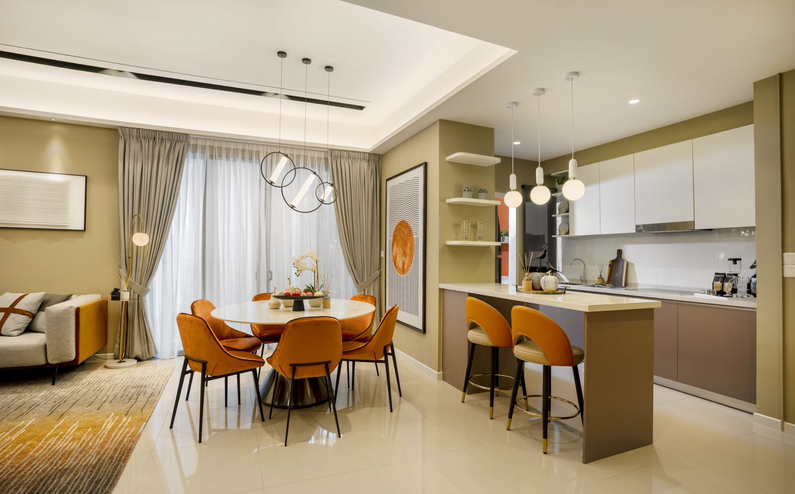 The dining area connects seamlessly to the kitchen through consistent flooring and ceiling heights, with orange upholstered chairs around a white circular table beneath geometric pendant lighting