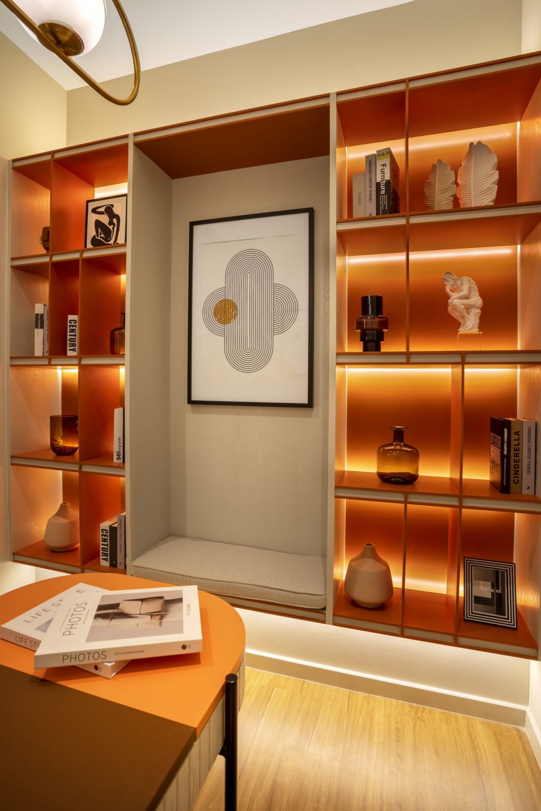 The home office’s orange-backed shelving with integrated lighting creates a striking focal point while providing practical storage