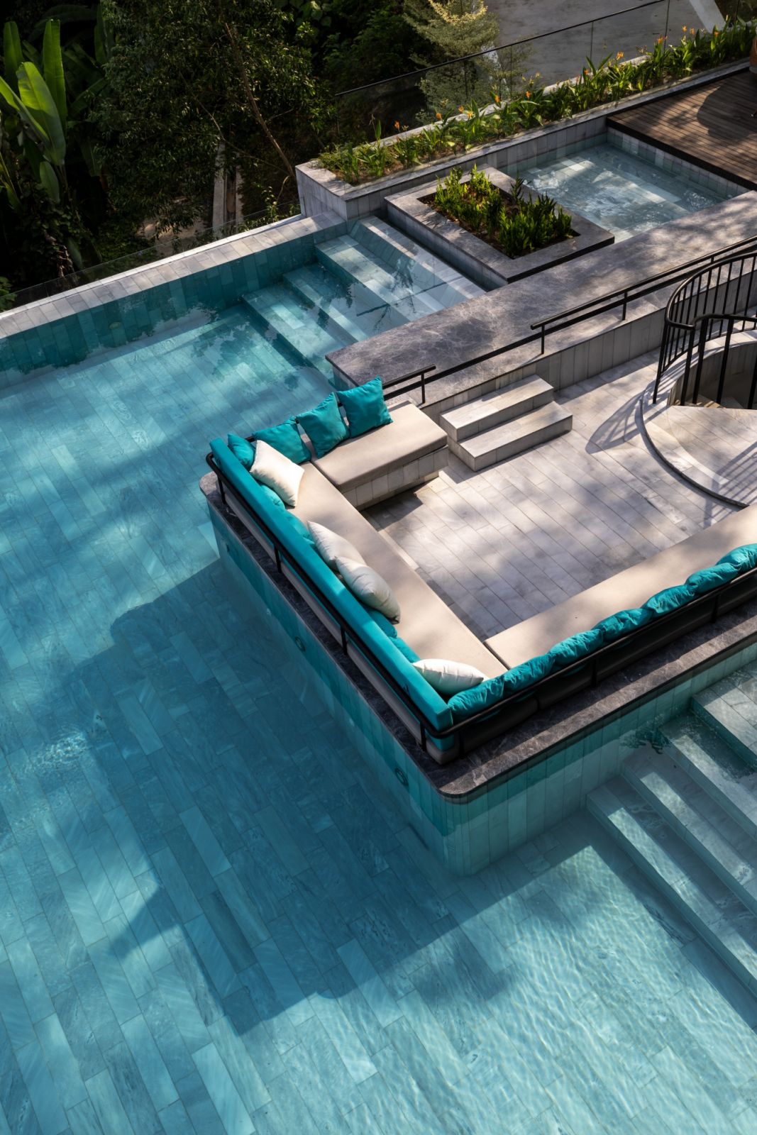 The resort-style pool area features a sunken seating area with turquoise cushions, exemplifying the seamless indoor-outdoor living concept