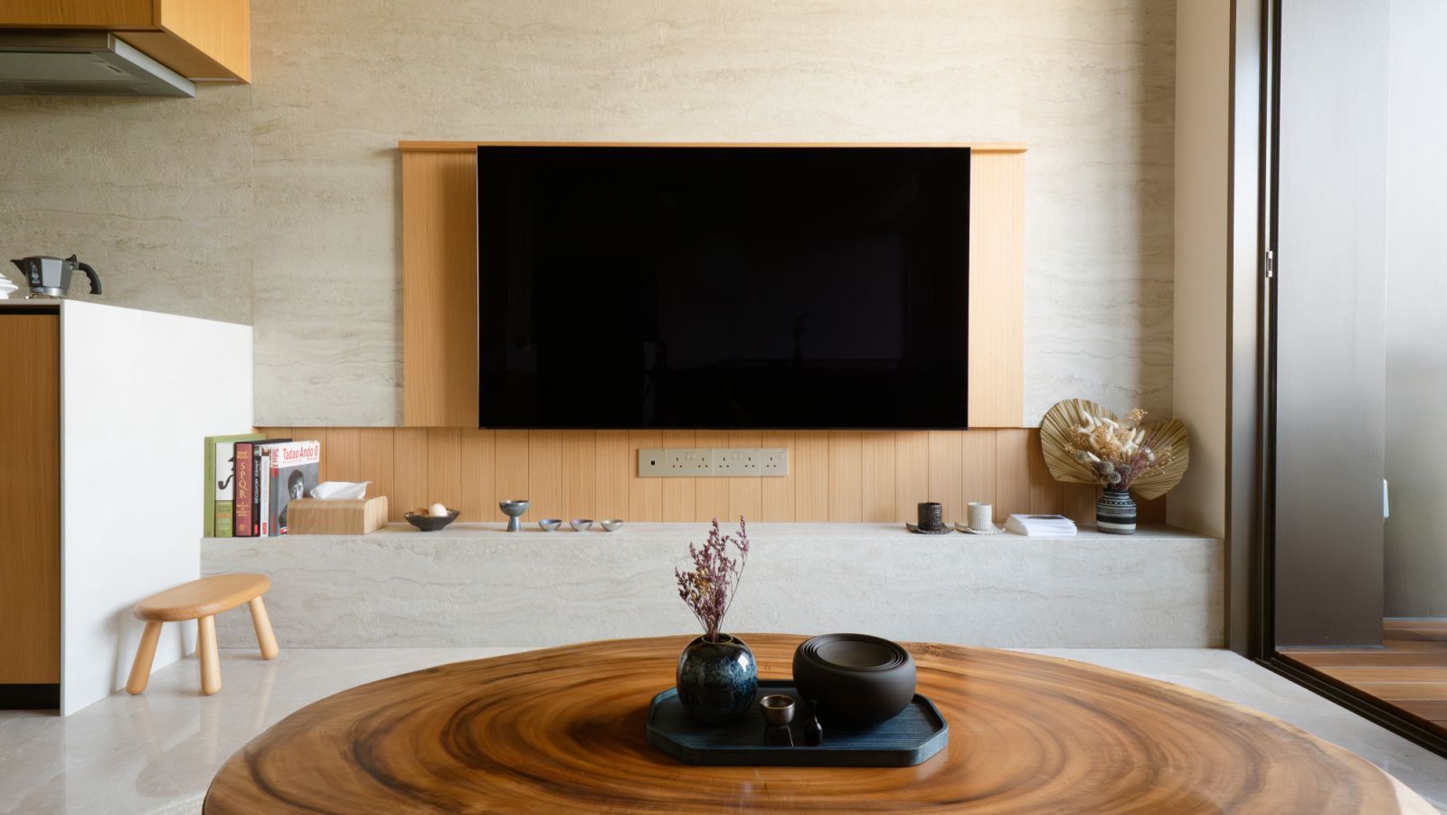 A monolithic stone and timber backdrop anchors the space, visually extending toward the balcony to amplify depth and openness