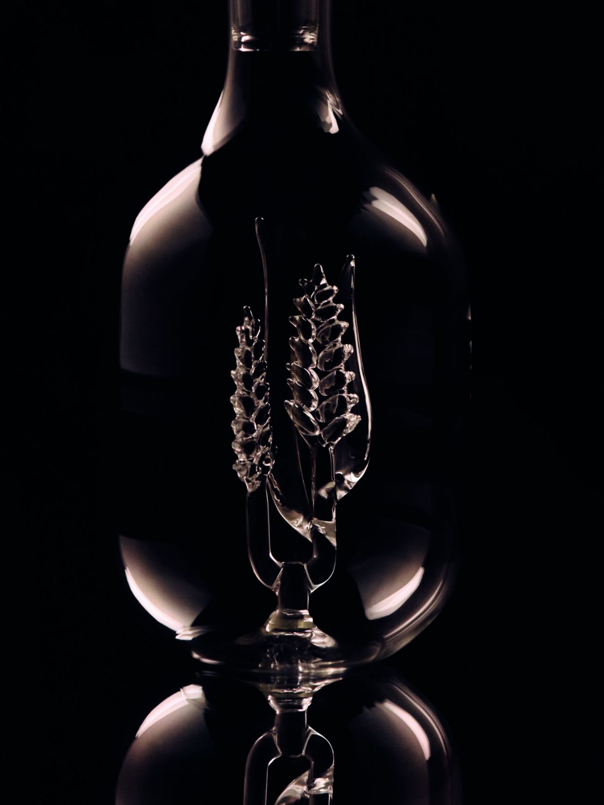A glass carafe with an intricate grain-like botanical sculpture on the inside of the vessel