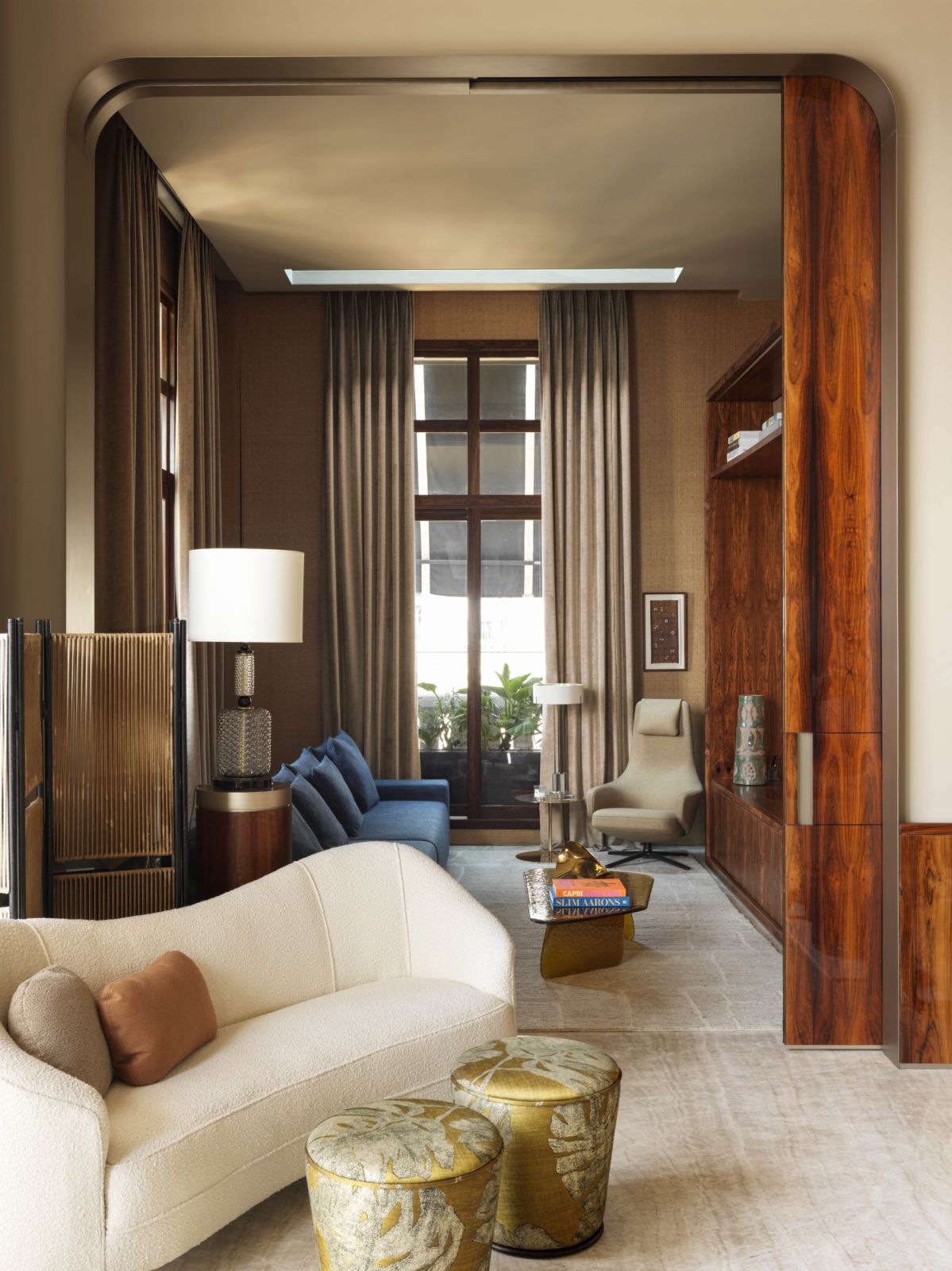 A view from the living room into the TV room reveals the Morfa No.7 glass coffee table by Lucas Recchia, a blue sofa from Micasa and an Italian art deco lamp