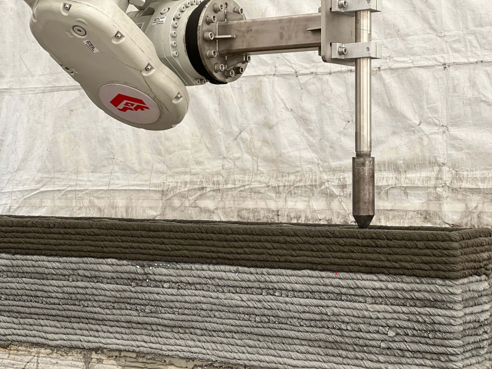 A close-up of CES_InnovFab’s robotic arm in action, layering wet concrete with precision and control that defines the tactile geometry of the 3D-printed house