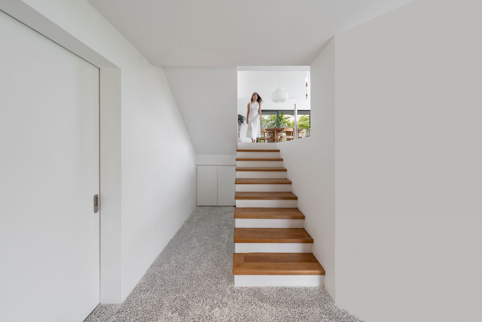 Split-level bungalow staircase design uses oak timber treads and terrazzo flooring to connect the ground floor study area with the upper living spaces in this Malaysian home