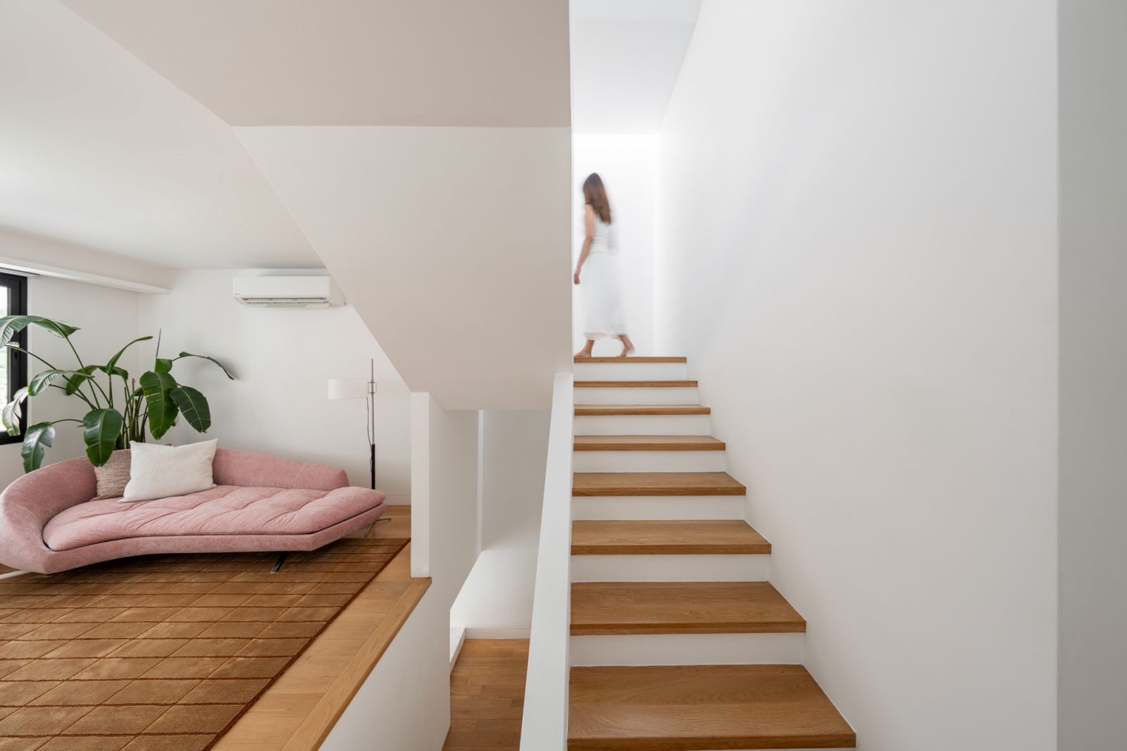 Split-level bungalow lounge area showcases oak timber flooring, integrated seating, and pink upholstered furniture connecting to double-height living spaces below