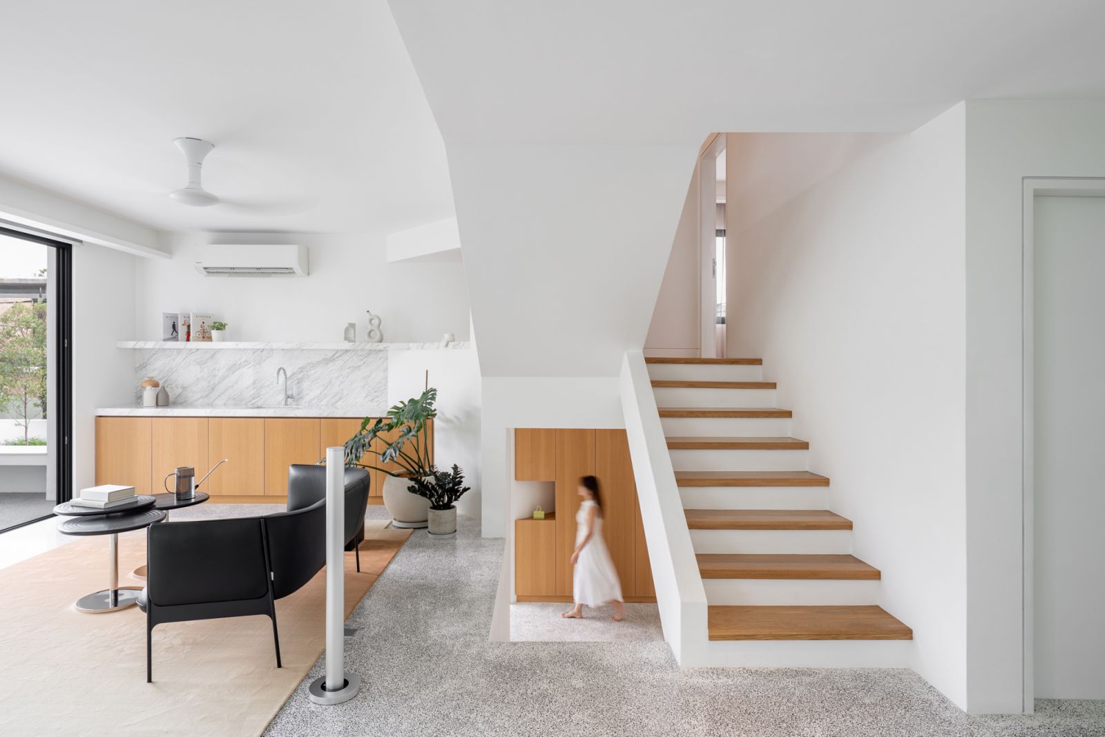 Bar lounge area beneath bungalow staircase utilizes angular geometry to create openings at mid-landings, connecting split levels with marble kitchen backdrop