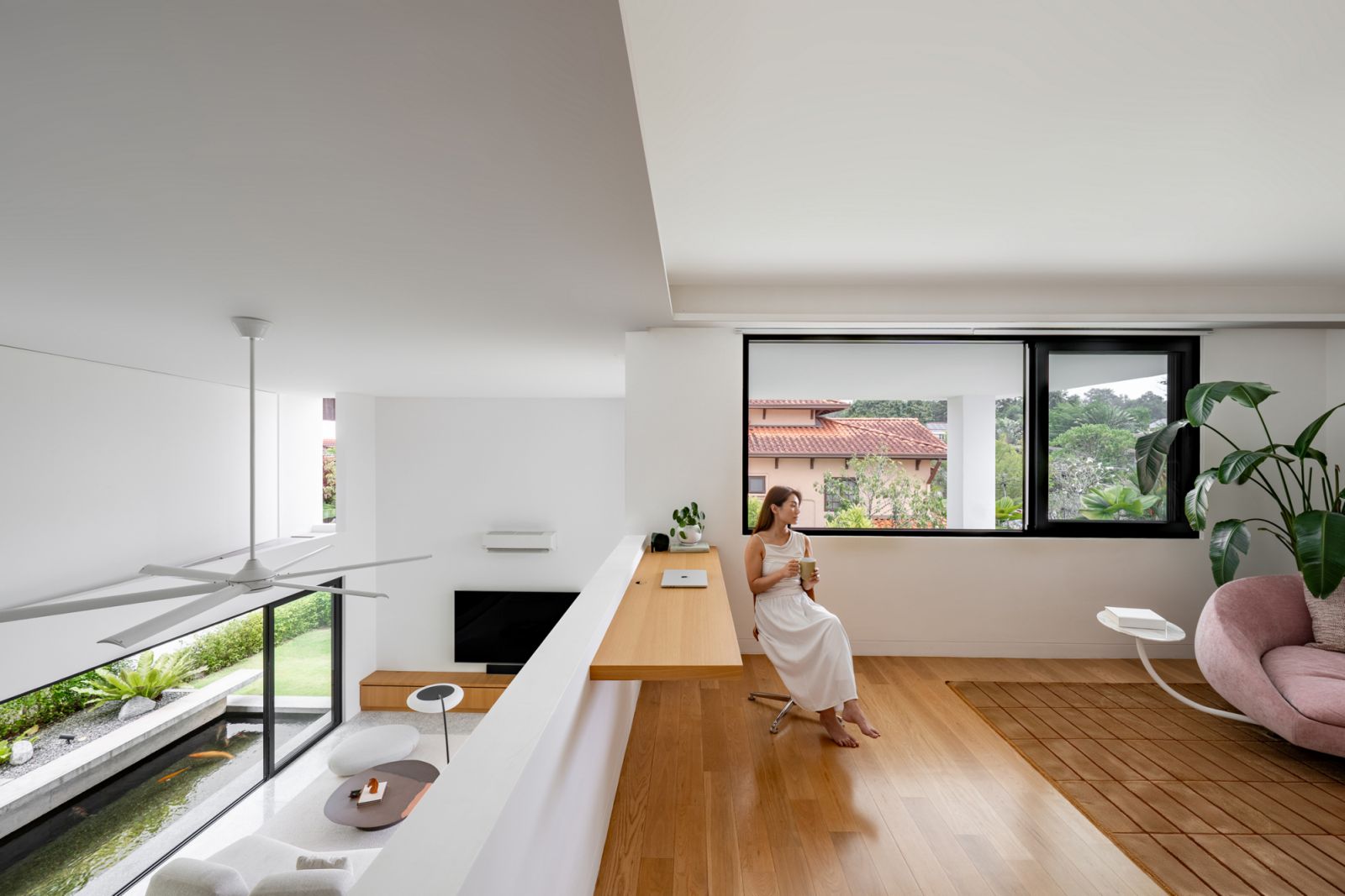 Upper level workspace in renovated bungalow features built-in oak desk overlooking double-height living area with seamless indoor-outdoor connection to garden