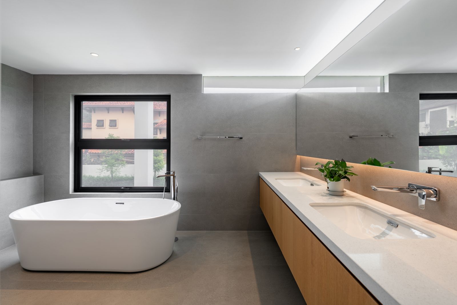 Master bathroom in renovated Kuala Lumpur bungalow features freestanding bathtub, warm timber vanity, and terrazzo flooring with views to neighbouring houses