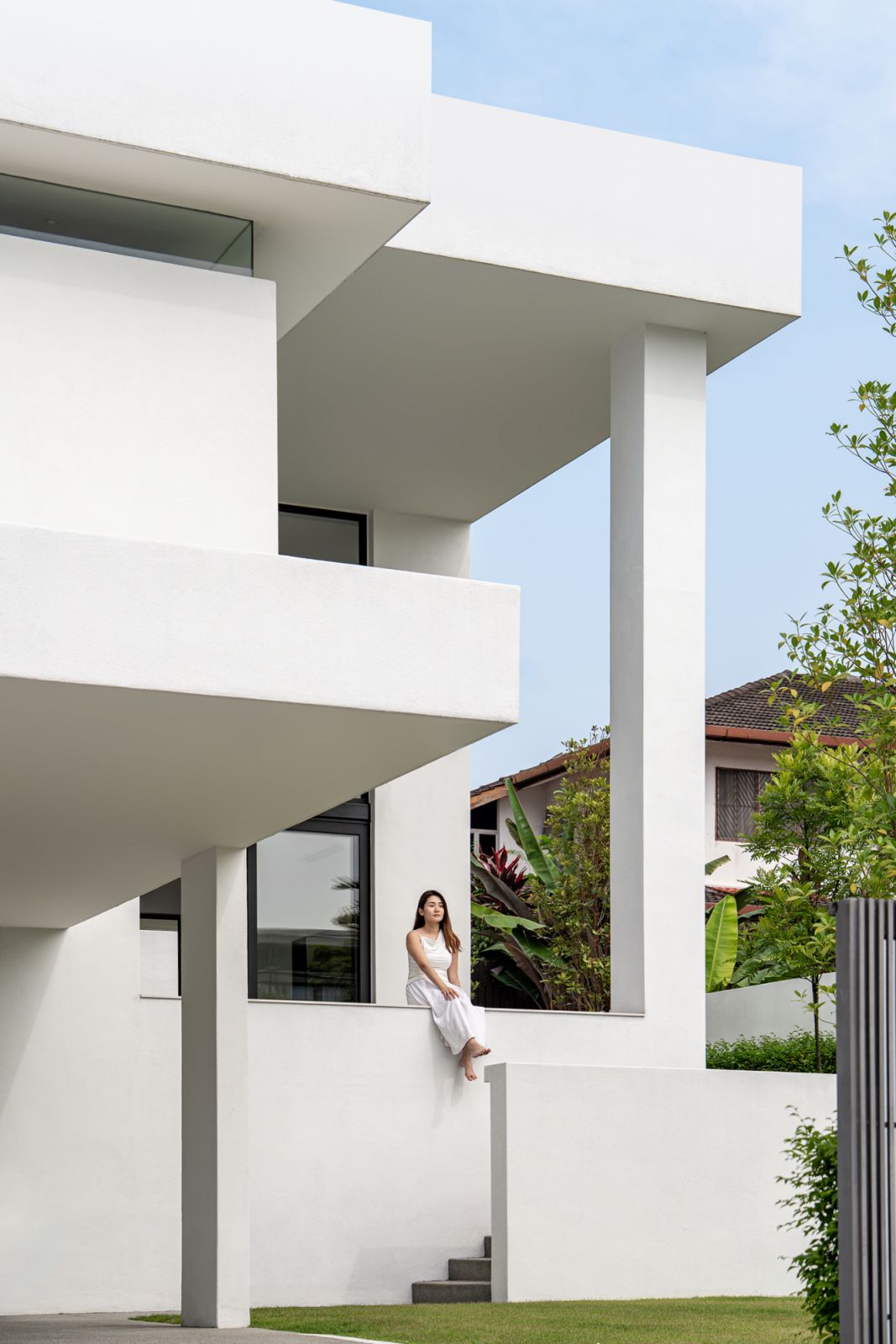 External staircase and elevated deck area of contemporary Kuala Lumpur bungalow renovation features integrated structural columns as seating, overlooking front garden with tropical landscaping