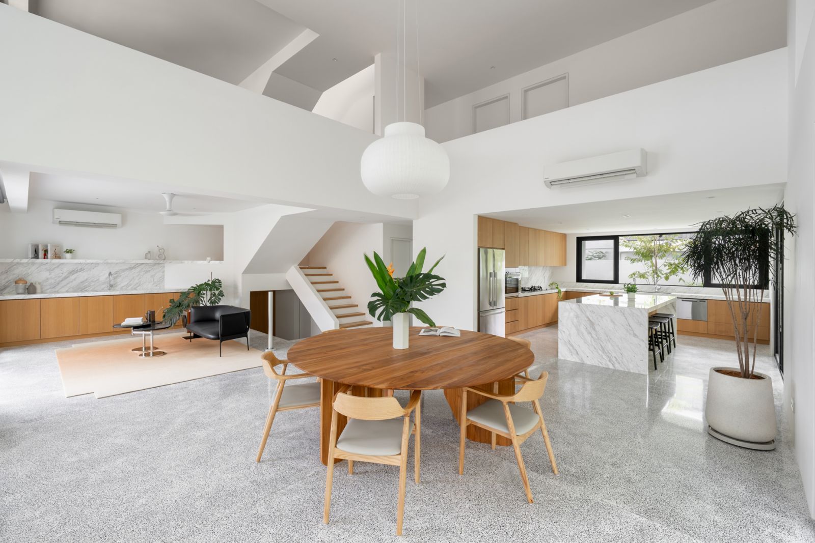 Open-plan bungalow interior combines dining, living, and kitchen areas with terrazzo flooring, timber accents, and double-volume ceiling design for tropical living