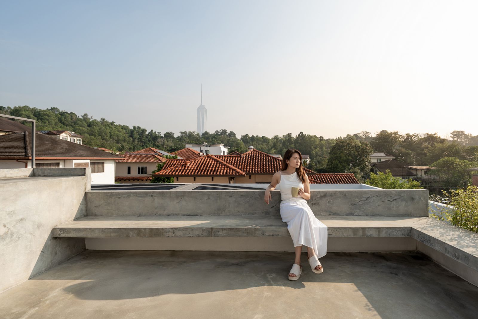 Rooftop terrace of hillside Kuala Lumpur bungalow offers panoramic neighbourhood views and integrated concrete seating with city skyline glimpses inthe distance