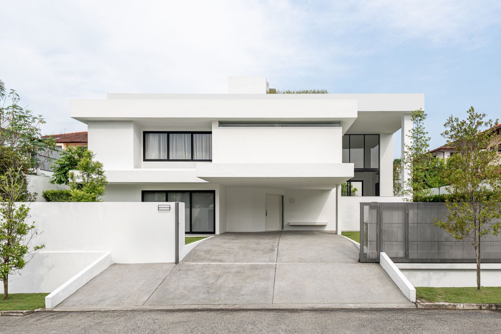 Street elevation of renovated Kuala Lumpur bungalow displays minimalist white architecture with black window frames and integrated carport on hillside plot