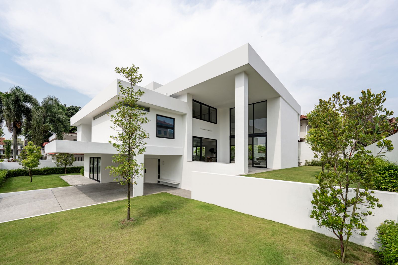 A garden view of the white contemporary bungalow showcases clean architectural lines, extensive glazing, and integration with tropical landscape design and lawn areas.