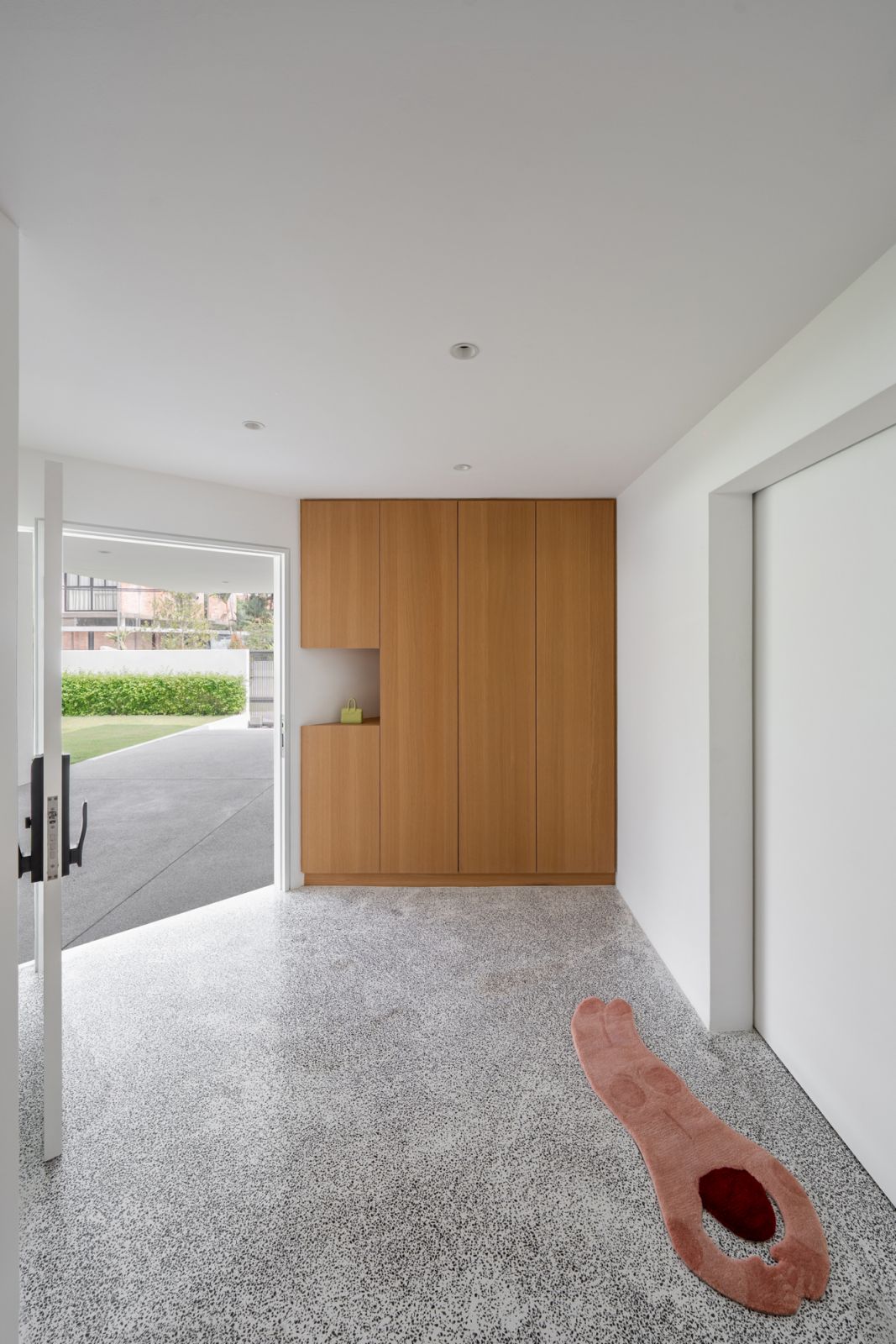 Entry foyer of the renovated Malaysian bungalow features built-in timber storage, terrazzo flooring continuation, and direct garden access through modern glass doors