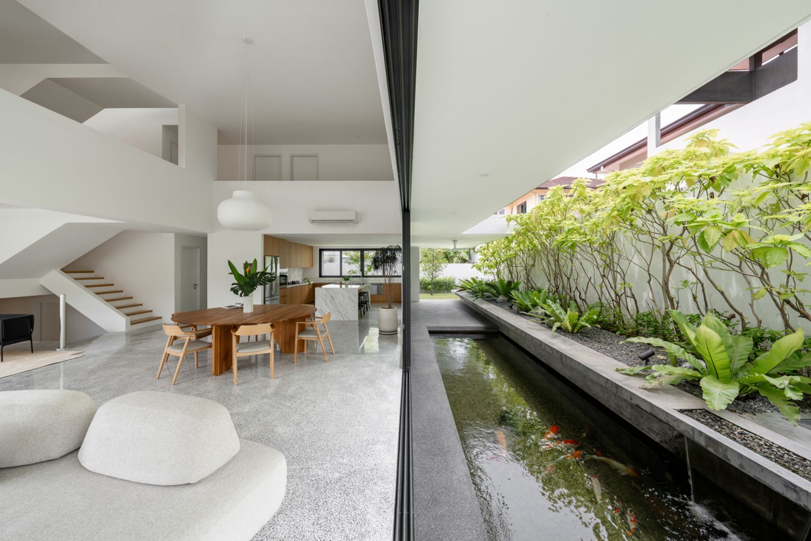 The living area of the split-level bungalow opens directly onto koi pond through sliding doors, with elevated concrete planters providing natural cooling and privacy screening