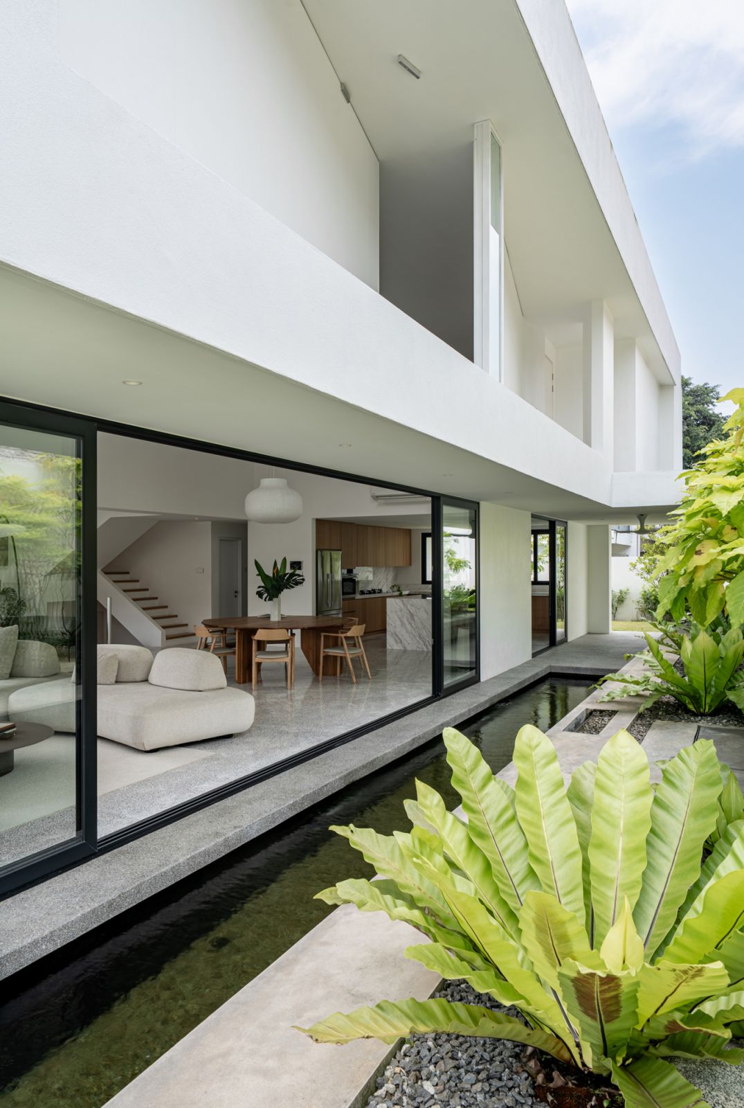 The Hillside bungalow’s exterior showcases a contemporary white façade with integrated landscaping, an elevated koi pond system, and tropical planting for natural cooling.