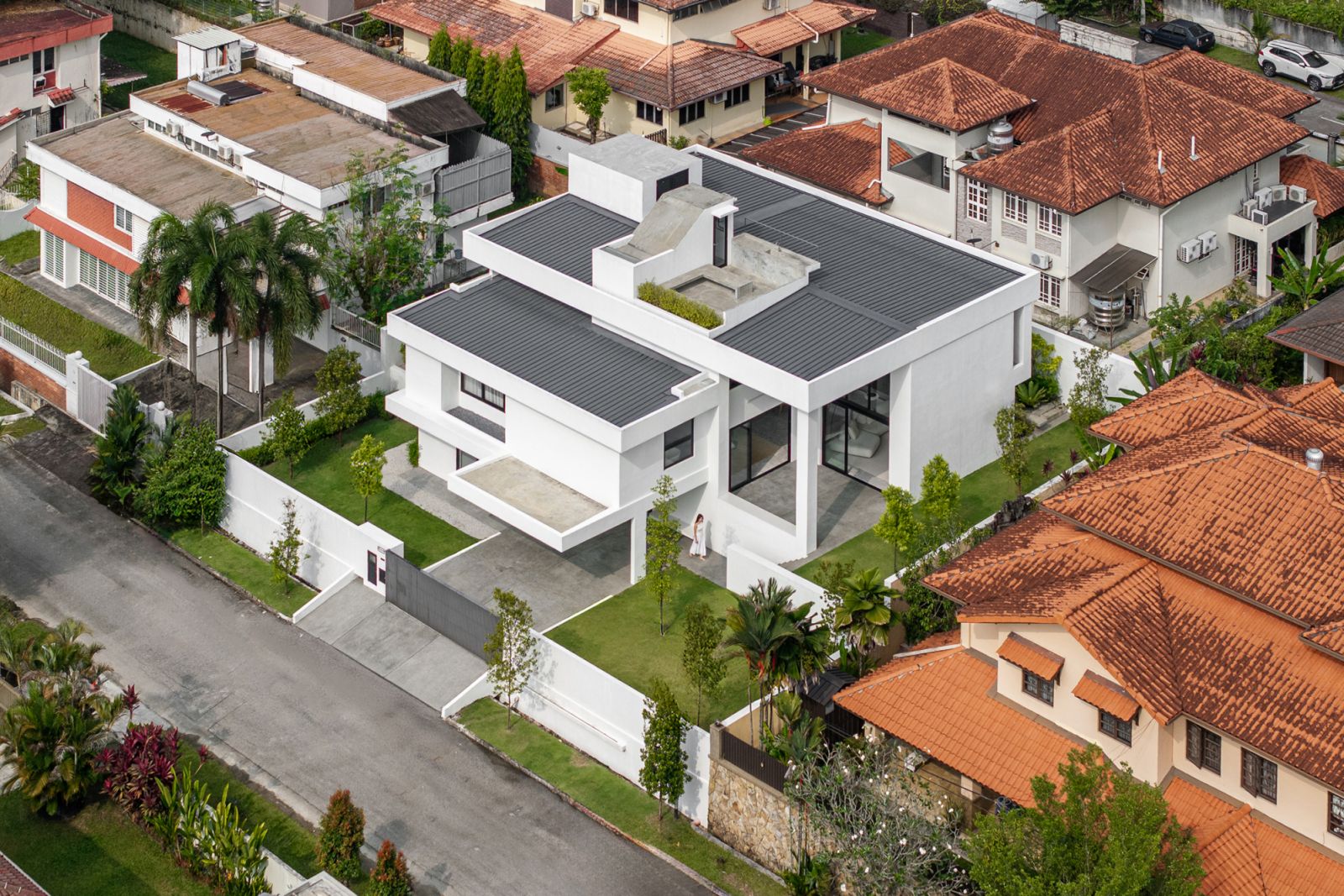 Aerial view of renovated bungalow on hillside plot shows relationship with traditional terracotta-roofed neighbours and contemporary white architectural intervention