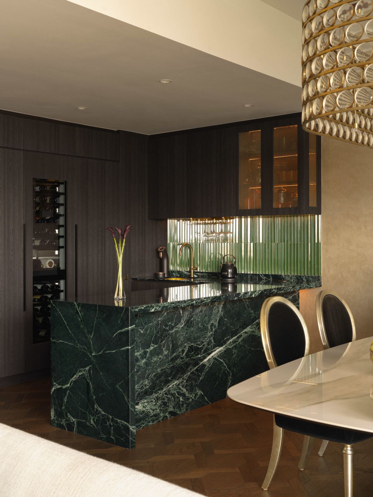 A green glossy tile backsplash, deep green marble island and dark cabinetry create an opulent yet cosy kitchen