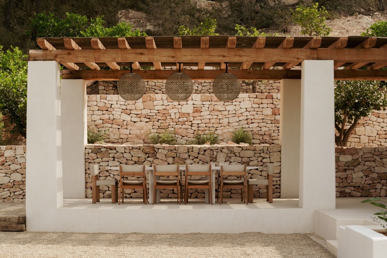 An outdoor dining pavilion combines traditional stone walls with contemporary woven pendant lights, creating a sheltered space that maintains the connection to the landscape