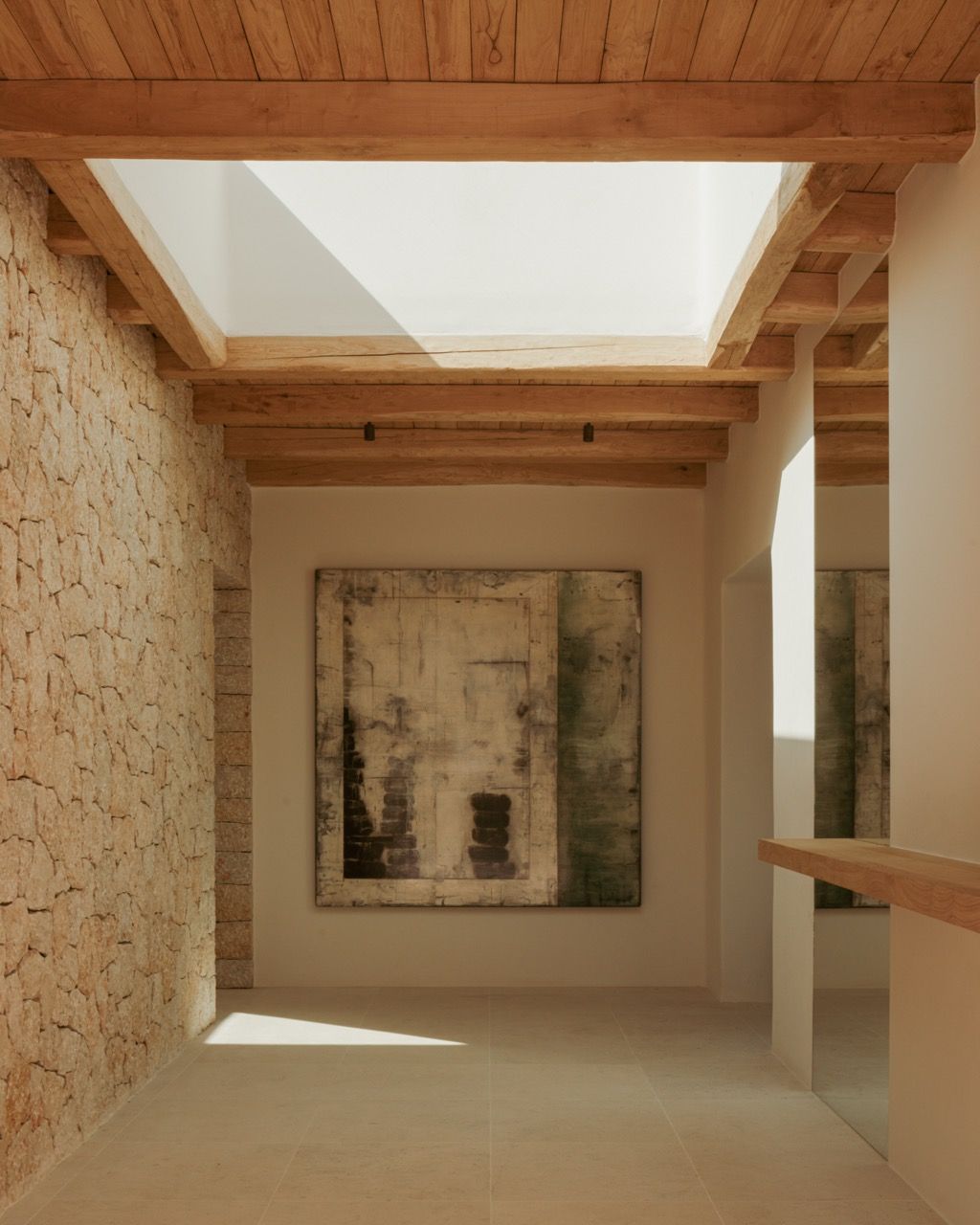 A skylight illuminates the hallway’s junction of traditional stone walls and exposed beams, with contemporary artwork providing a focal point in the carefully curated space