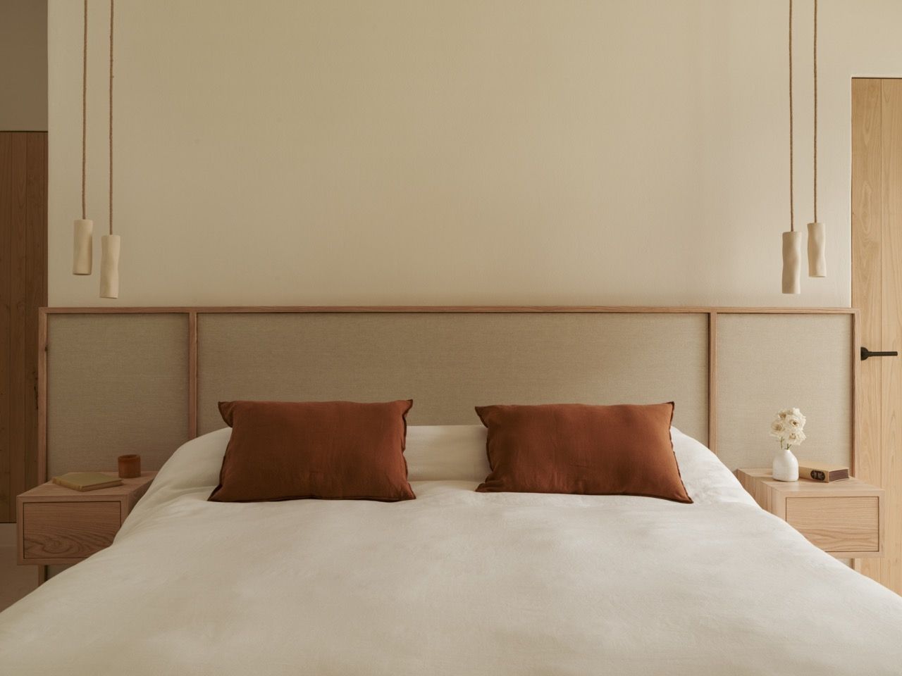 A guest bedroom demonstrates the consistent design language throughout the house, with custom wooden headboards and terracotta accent cushions adding warmth to the neutral scheme