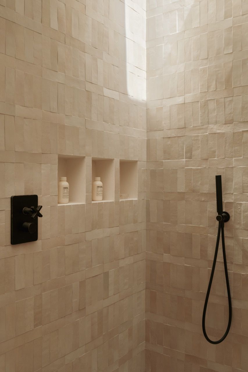 The shower features traditional sandstone tiles with built-in storage niches, combining practical functionality with the home’s commitment to natural materials and clean lines