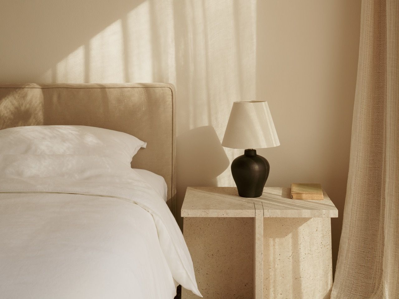 The master bedroom features a custom bed frame designed by Tom Lawrence-Levy in neutral fabrics, with natural stone nightstands and sheer linen curtains that filter Mediterranean light