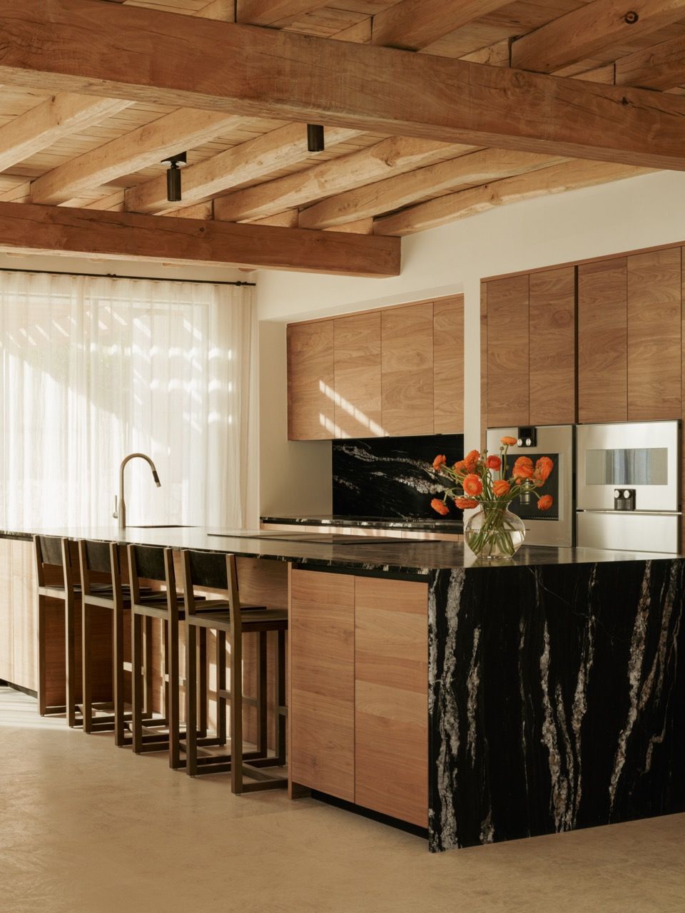 The kitchen features dramatic black marble island surfaces contrasted with warm wooden cabinetry, all beneath the traditional exposed beam ceiling structure