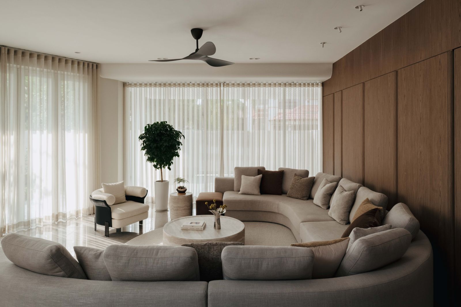 Curved living room seating area with natural veneer backdrop and large windows that transform the mood of the house throughout the day with changing light