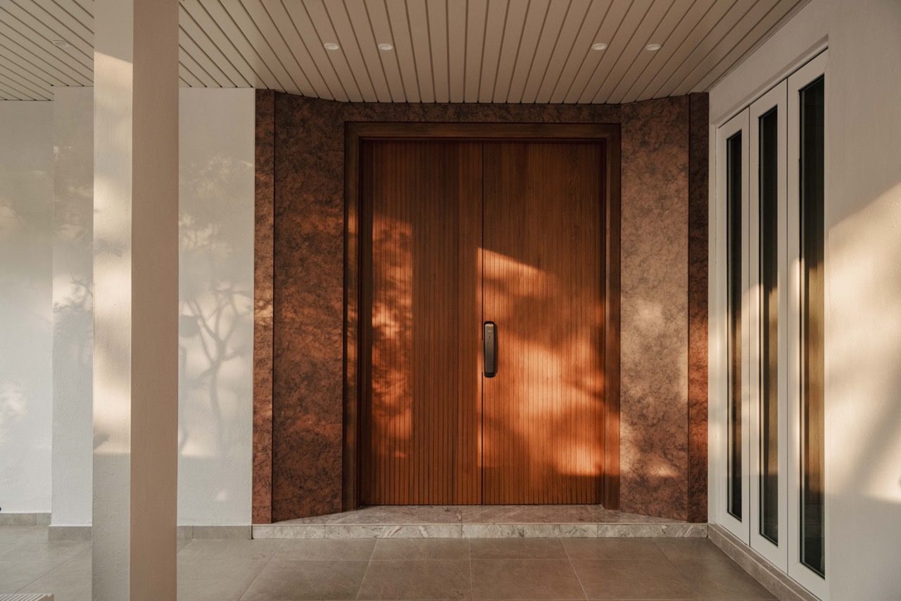 Entrance area with natural wood door and stone framing, demonstrating the welcoming arrival experience created by relocating the main entrance to the side.
