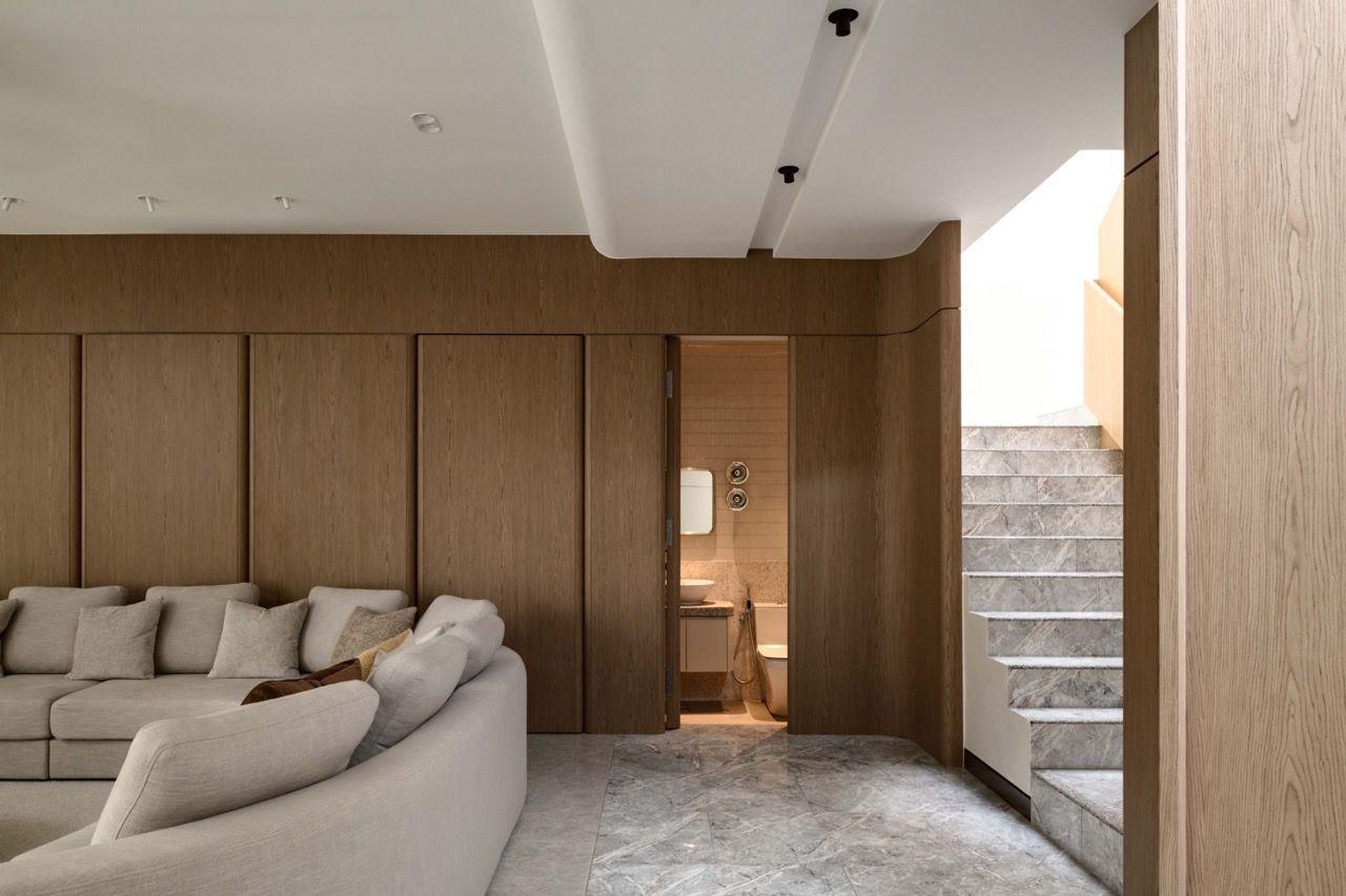 Living area with natural veneer wall panels and marble staircase visible, showing the connection between different levels through the central void