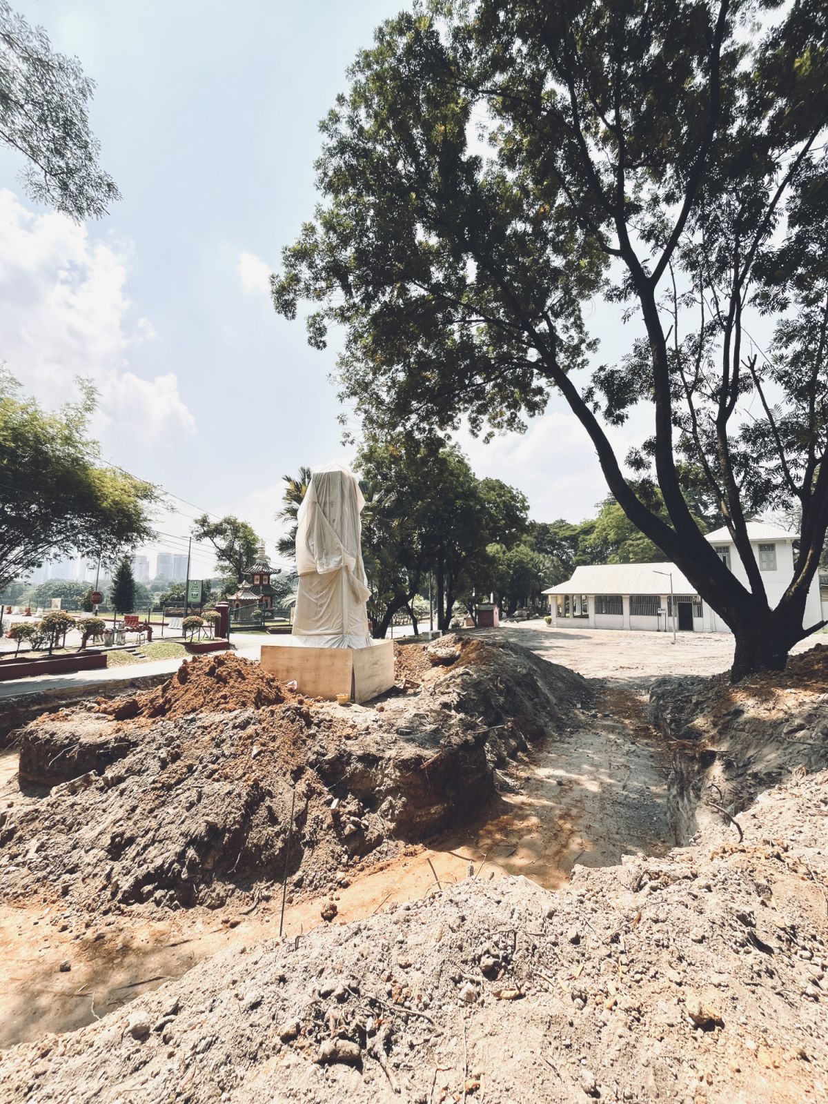 Site preparation reveals the memorial’s integration with the existing cemetery landscape, with the covered monument visible in the background as construction begins