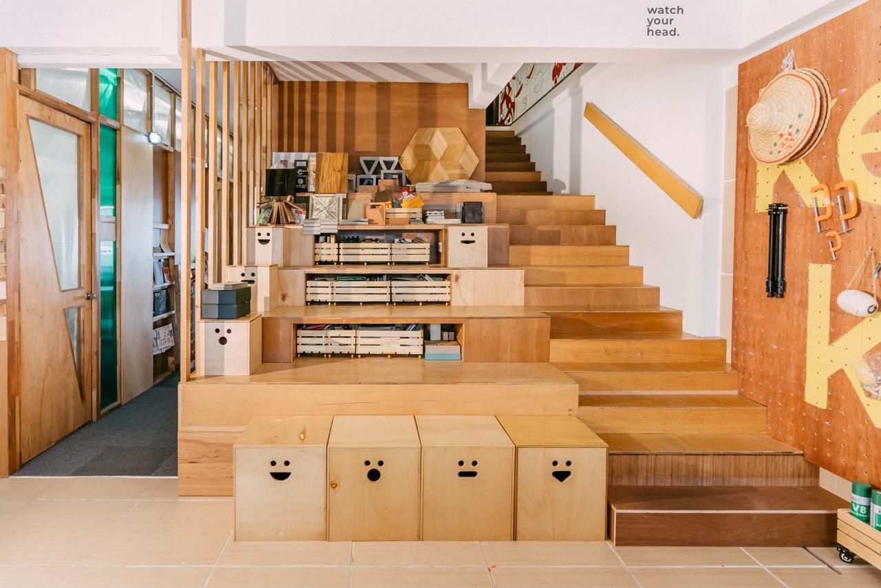 Ground floor workspace showing custom timber storage solutions integrated into the staircase design, with playful smiley-face storage boxes that reflect the studio’s hands-on, human-centred approach