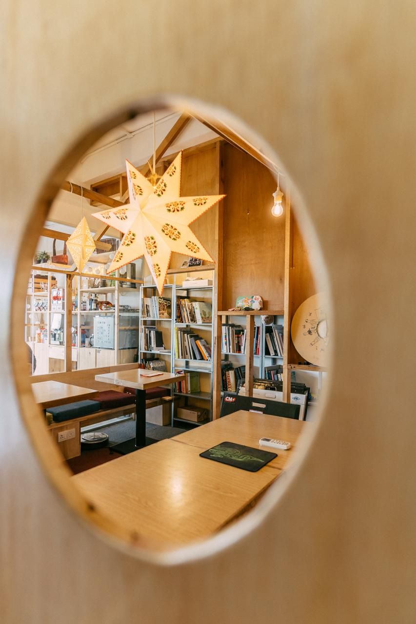 Interior view through a circular opening into the collaborative workspace, showcasing the studio’s library and meeting areas with exposed timber structure and traditional star-shaped lanterns creating warm, intimate spaces