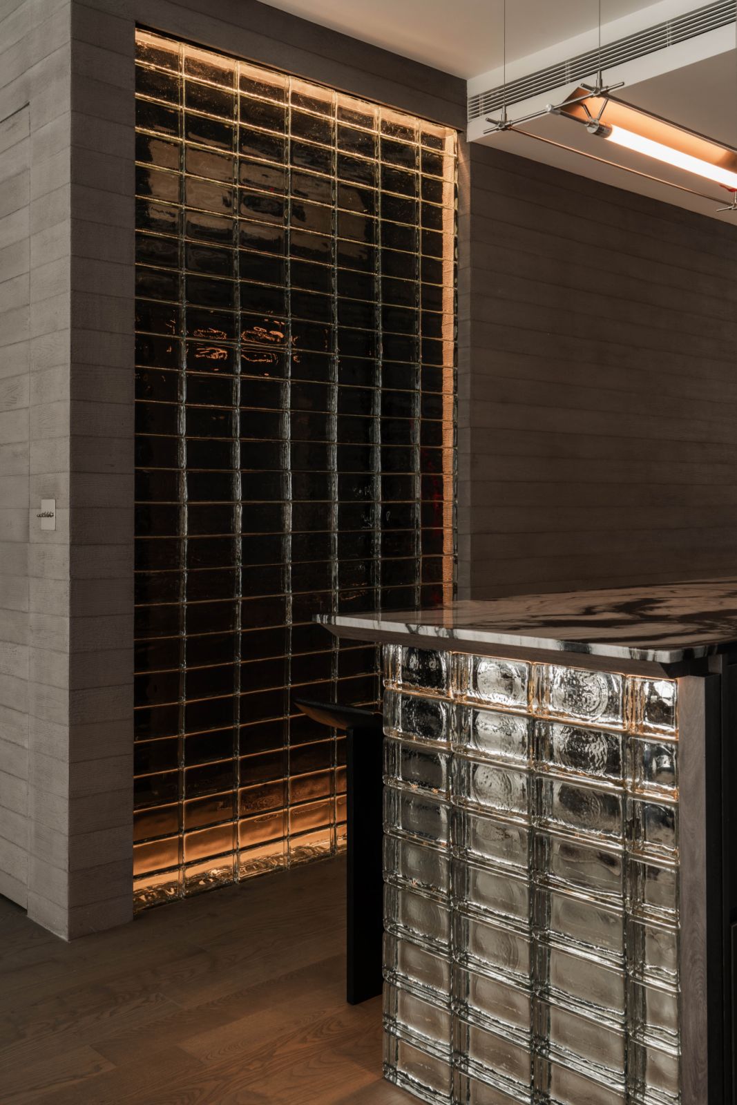 A marble island, resting on a luminous base of the same glass blocks, anchors the kitchen like a sleek centrepiece
