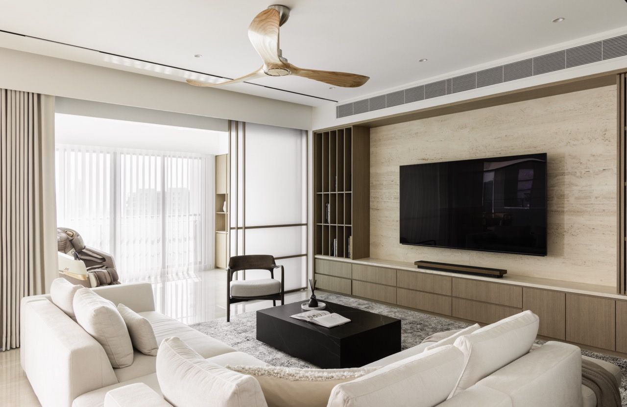 A cream sectional sofa anchors the space, with the travertine TV wall and timber shelving creating a sophisticated backdrop