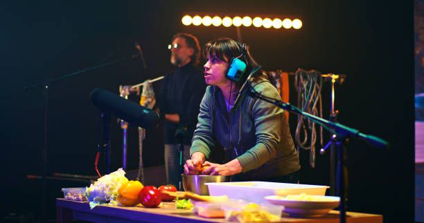 Determined woman cutting and squeezing orange over bowl near mature male colleague clinking metal chains while creating soundtrack for film in studio