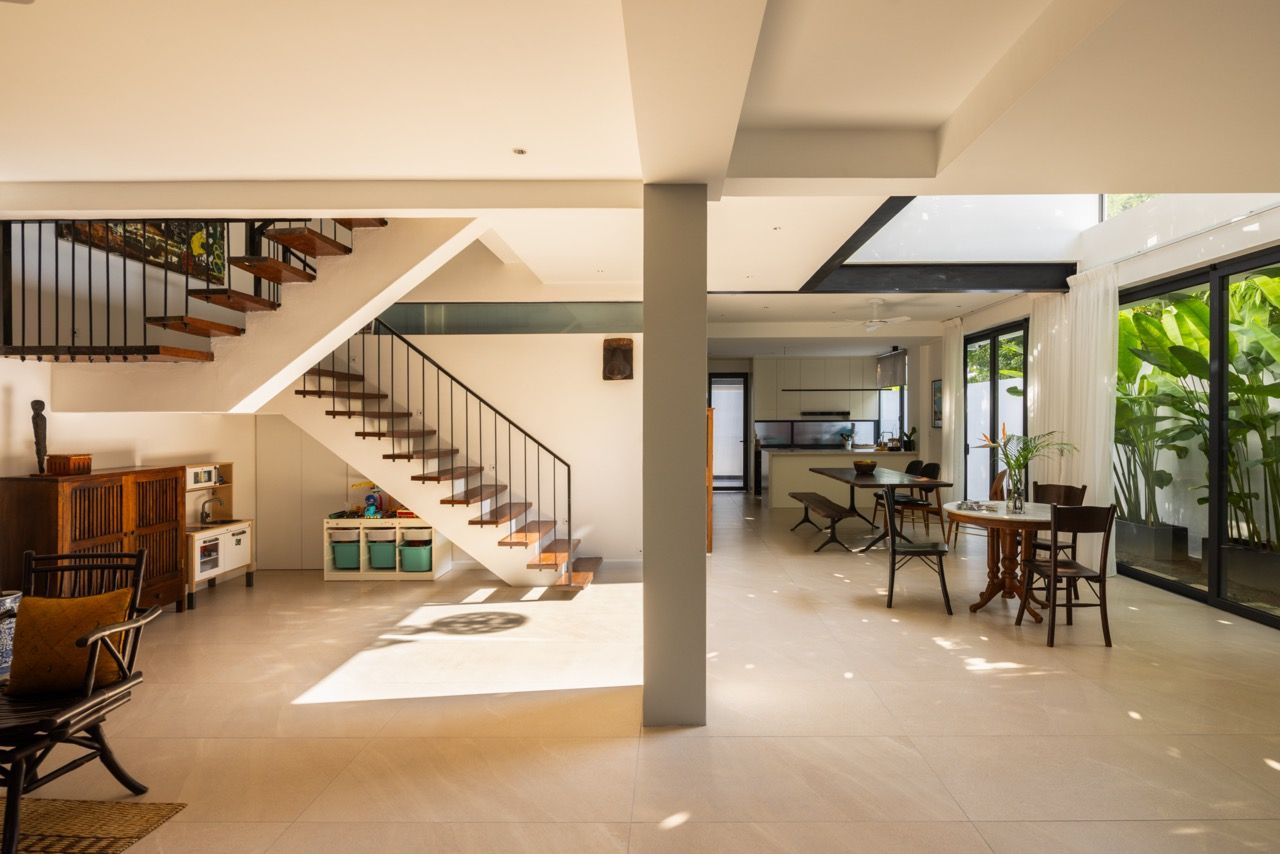 The ground floor’s open-plan living space showcases the floating timber staircase and double-height ceiling, with the family’s travel-collected furnishings integrated into the contemporary design