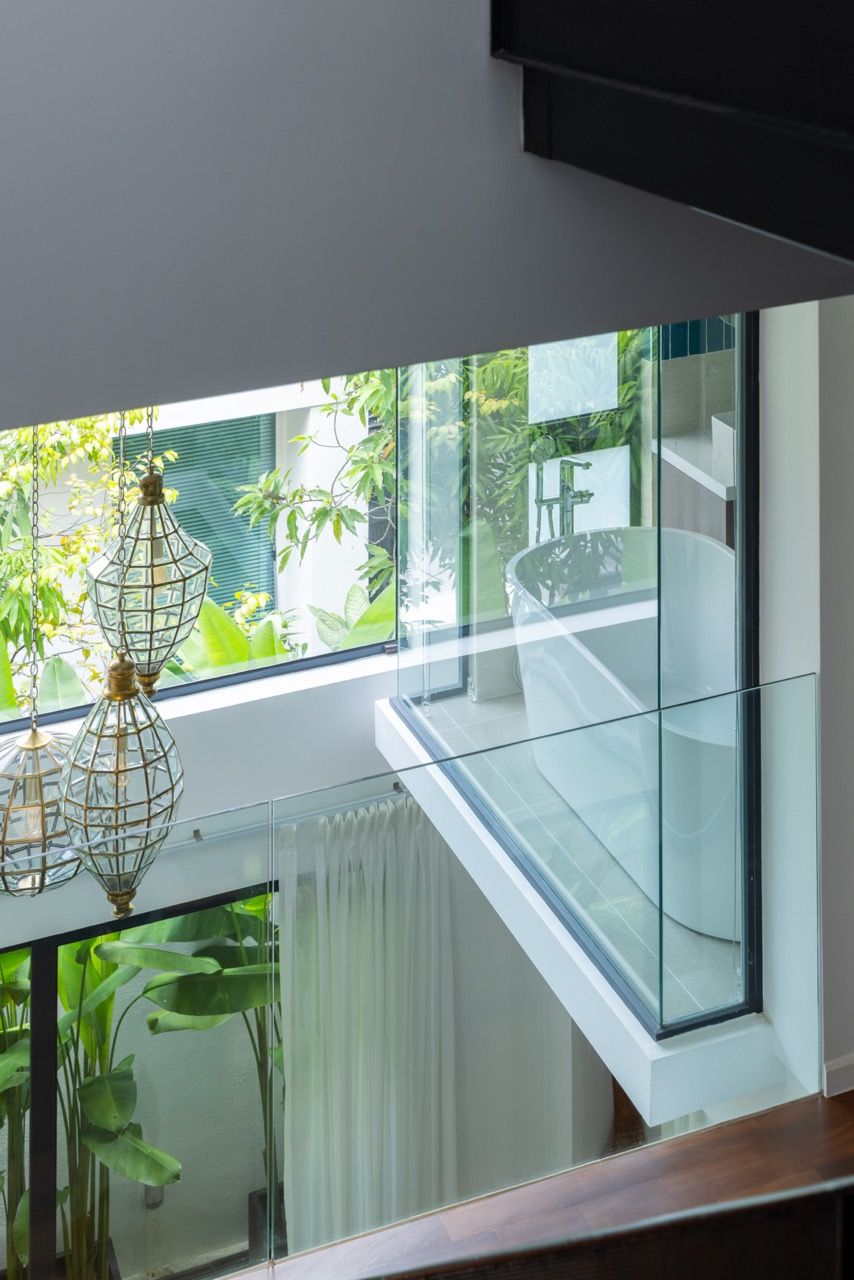 Custom brass pendant lights illuminate the suspended bathtub, with views through the glass walls to the garden beyond