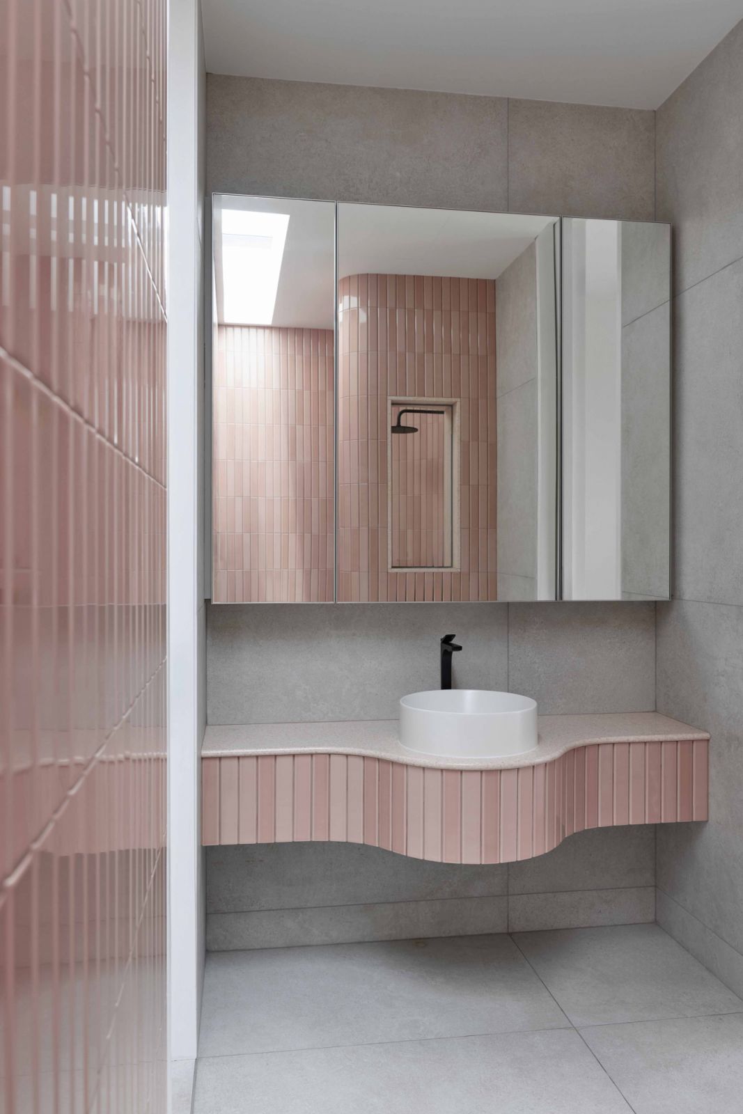 The playful curve of the pink-tile-clad bathroom counter lends softness and freshness to this powder room