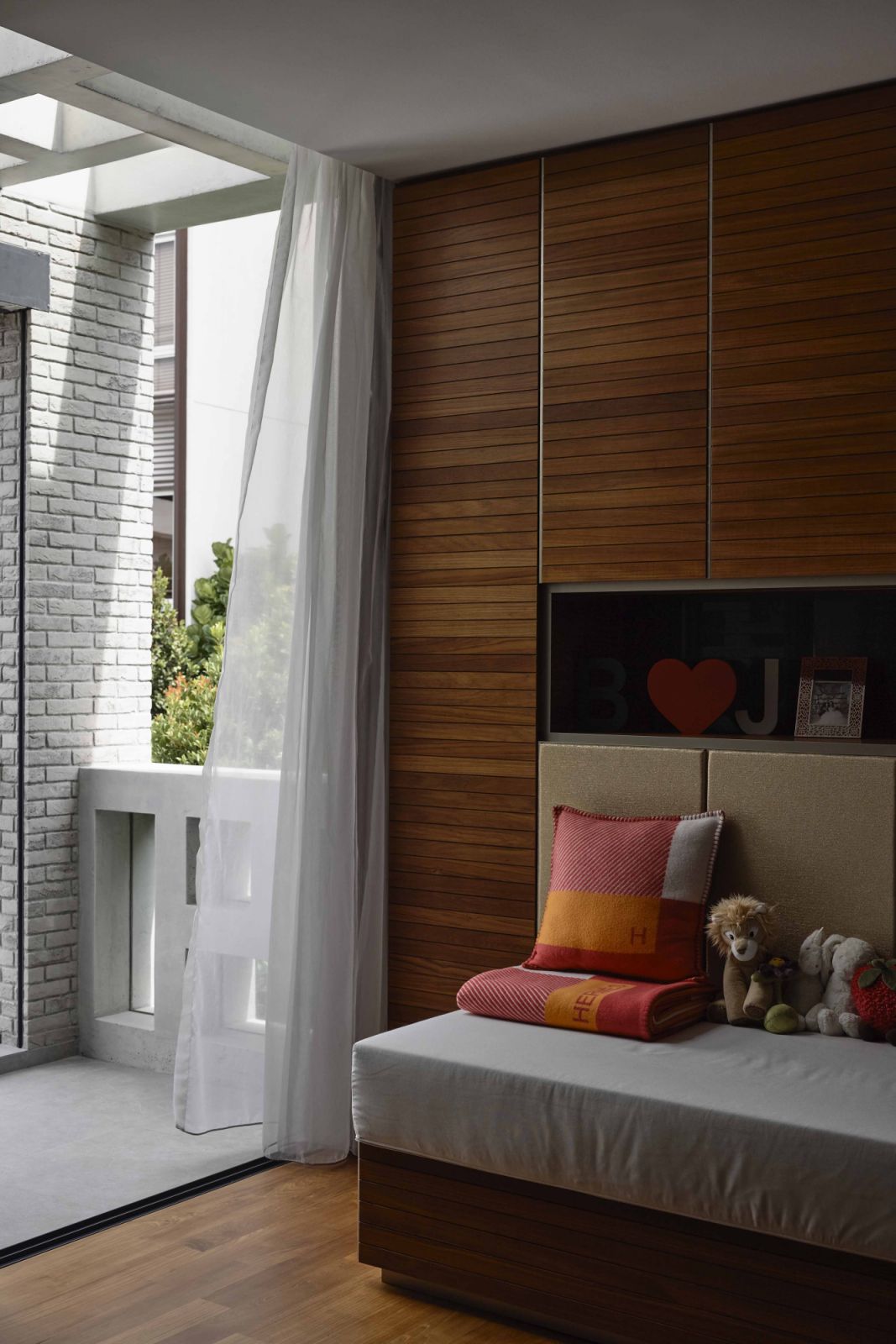 Curtains, warm timber finishes, and soft furnishings in a sunset-hued palette balance the coolness of the concrete and brick exterior