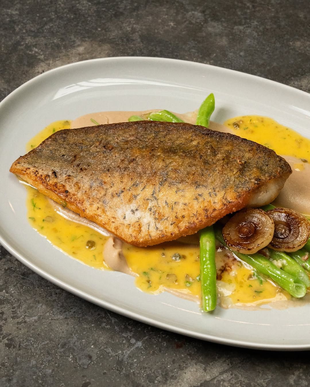 Sea Bass a la meuniere with smoked cauliflower puree and duck bacon confit cipolli (Photo: Instagram / @restaurantdominic)