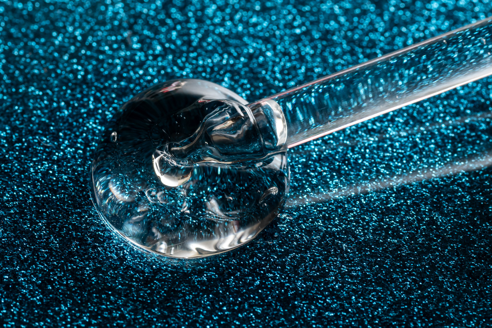 close up macro of pipette dropper with liquid serum on a glittering blue background luxury serum concept