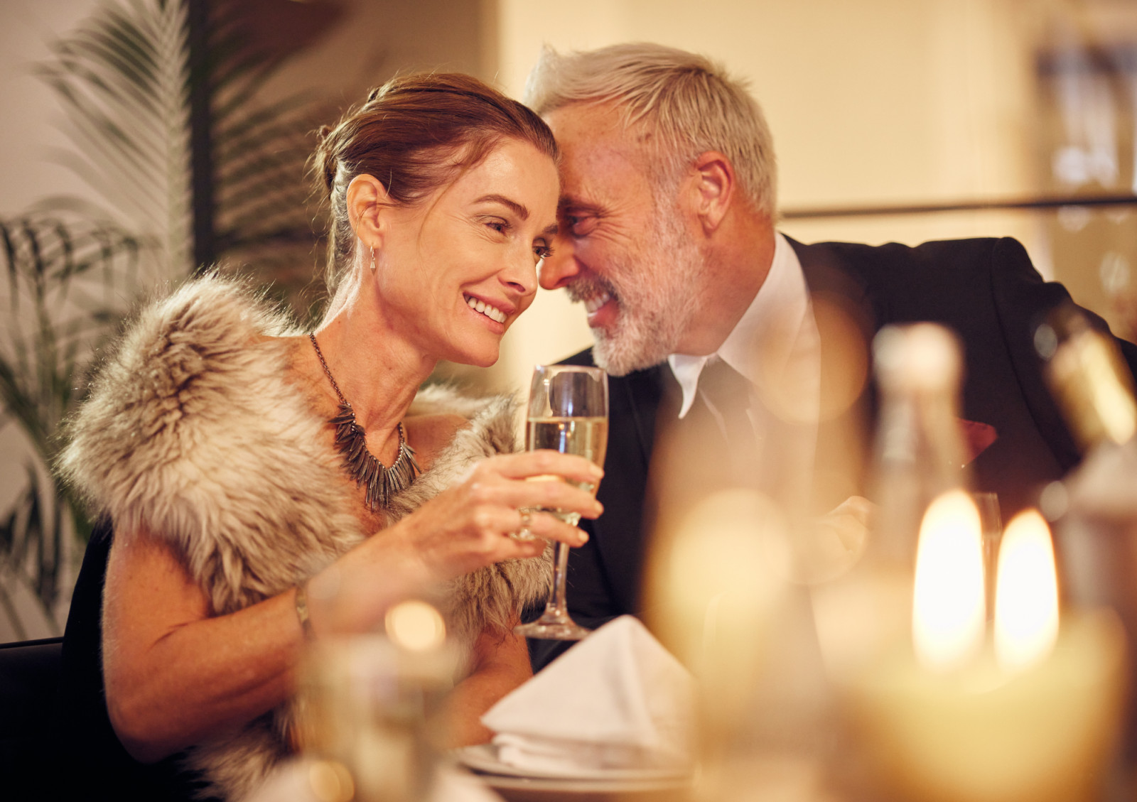 Woman, man and whisper at dinner, party or restaurant for celebration in night with smile, happy and gossip. New year, fine dining or gala event with champagne, conversation and romantic secret love.