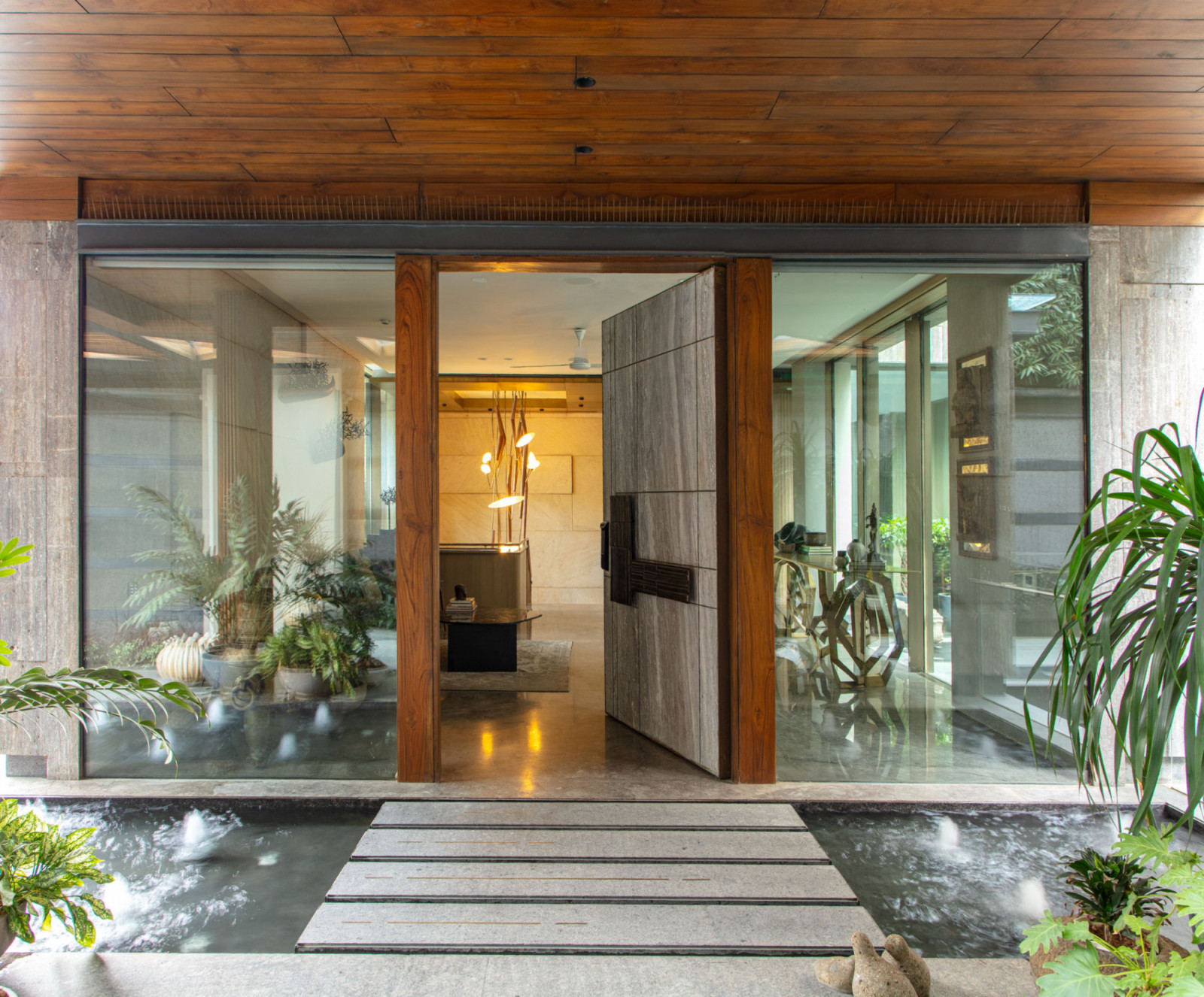 The entrance features a water element with stepping stones leading to glass doors framed in warm wood