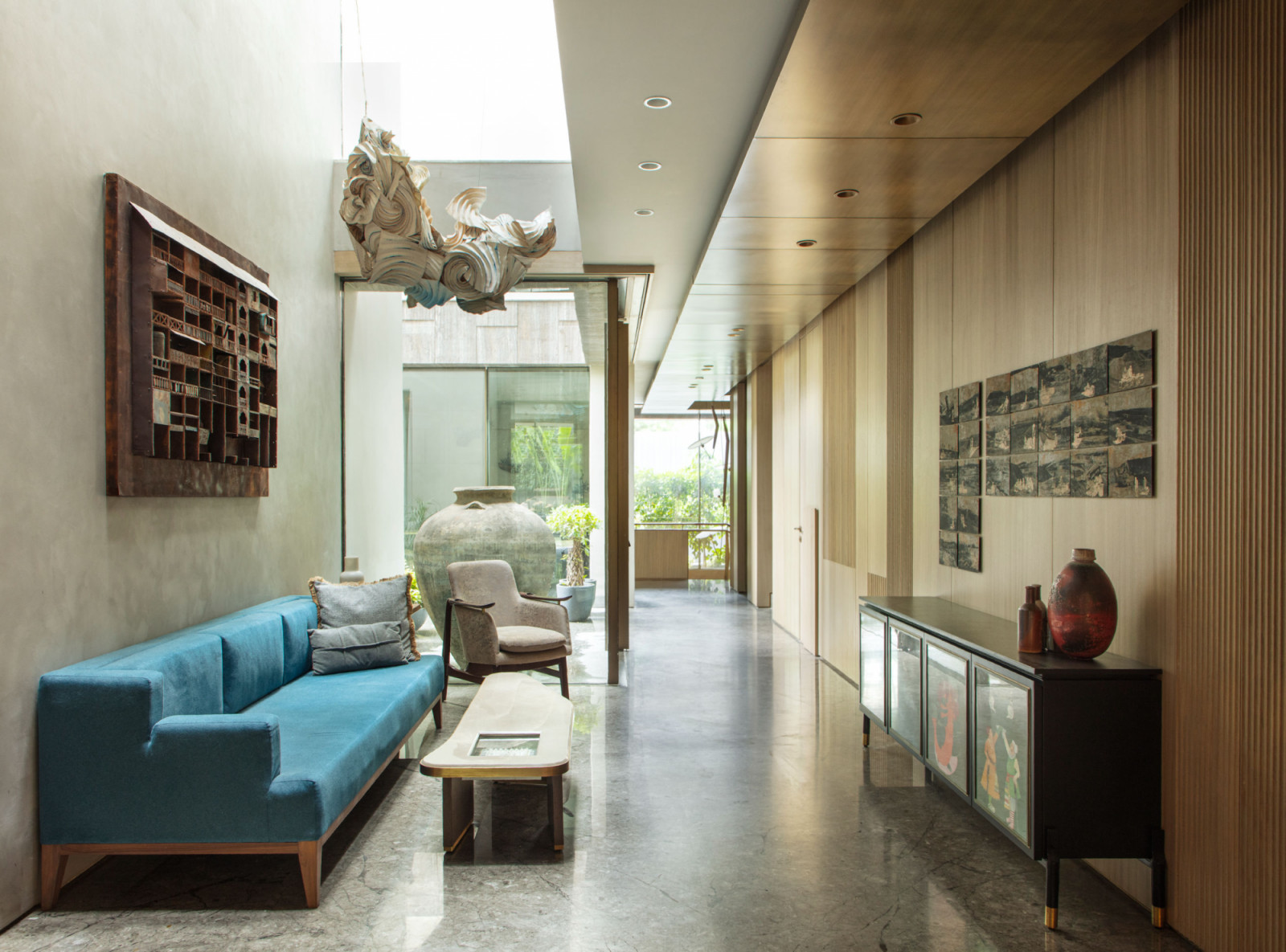 A bright hallway connects different zones of the house, featuring a turquoise sofa that breaks from the grey and cappuccino design palette, while a suspended origami installation creates visual drama overhead