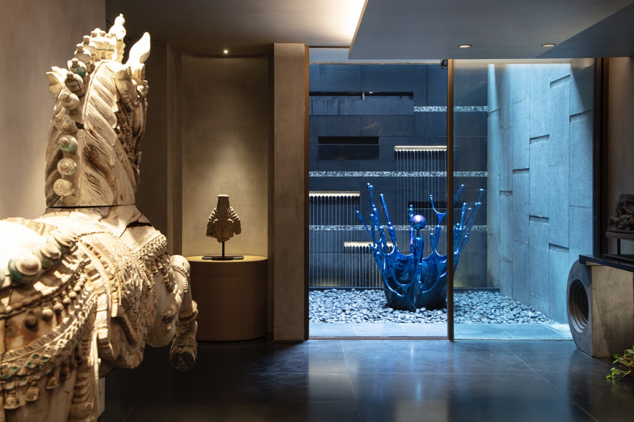 Traditional carved sculptures anchor spaces throughout the home, positioned alongside contemporary materials such as glass and steel