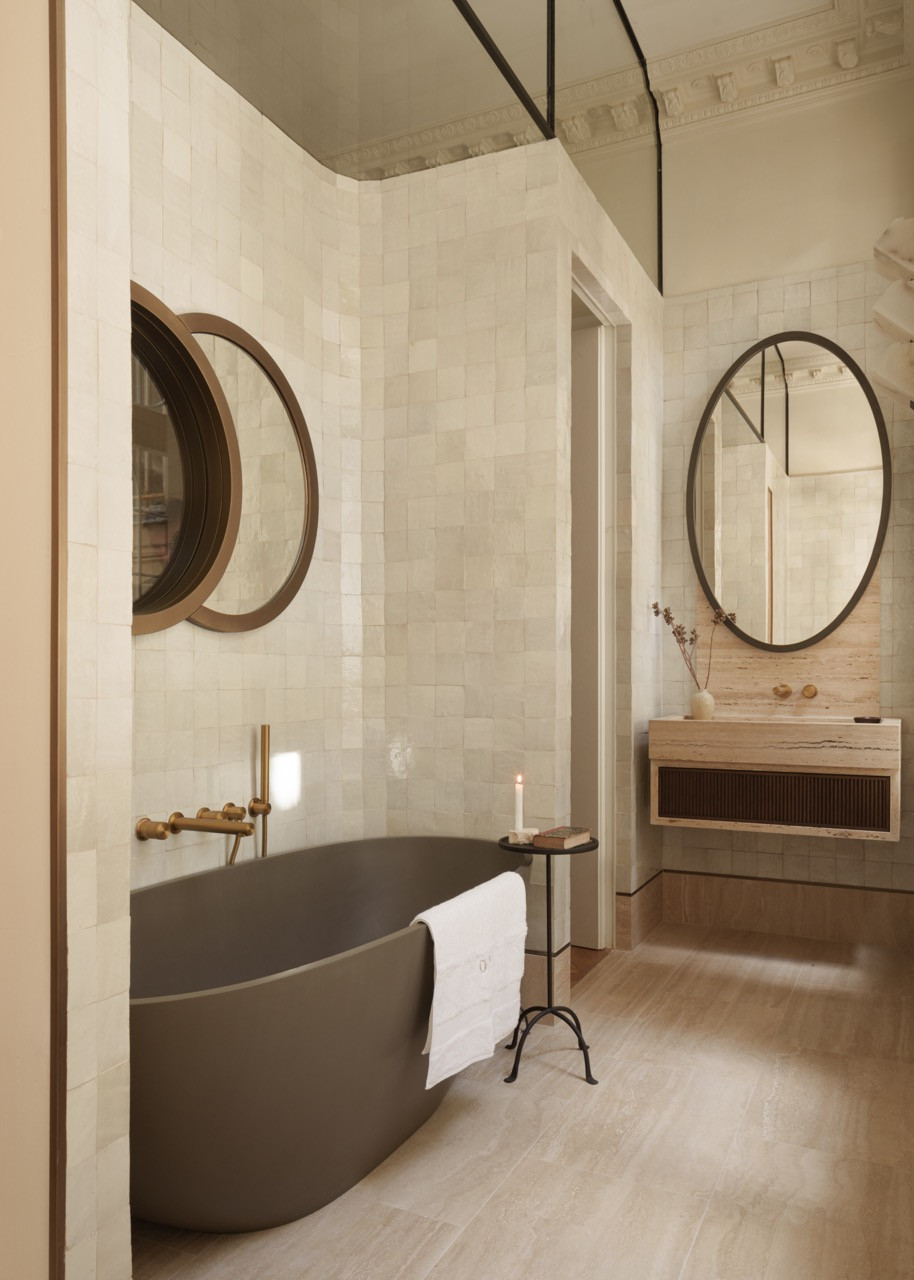 The main bathroom's travertine surfaces and custom vanity showcase the material continuity strategy, with the basin unit representing one of the spaces where travertine runs throughout the entire project