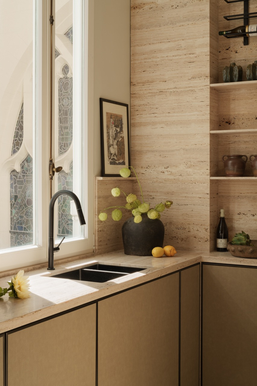 Travertine continues throughout the apartment as a unifying element, appearing in the kitchen backsplash and counters as part of the cohesive material strategy