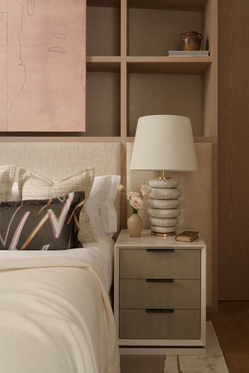Custom bedside storage showcases the apartment's textural approach, with built-in shelving displaying curated objects alongside tone-on-tone wallpaper featuring subtle white and pink flowers